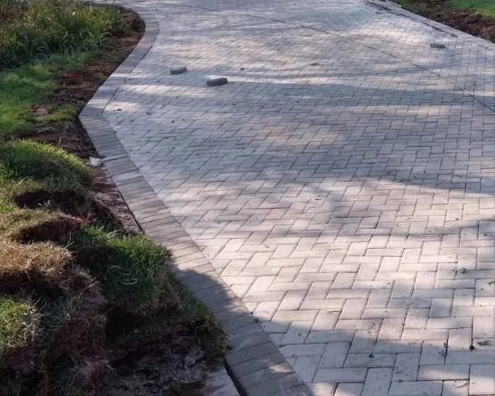 Driveway Paving: Materials, Costs and What to Expect 1 Grey bevel pavers newly laid in a 45 degree herringbone across a residential driveway, closed along its curved edge by a soldier course of the same pavers set on edge against freshly turned soil and grass