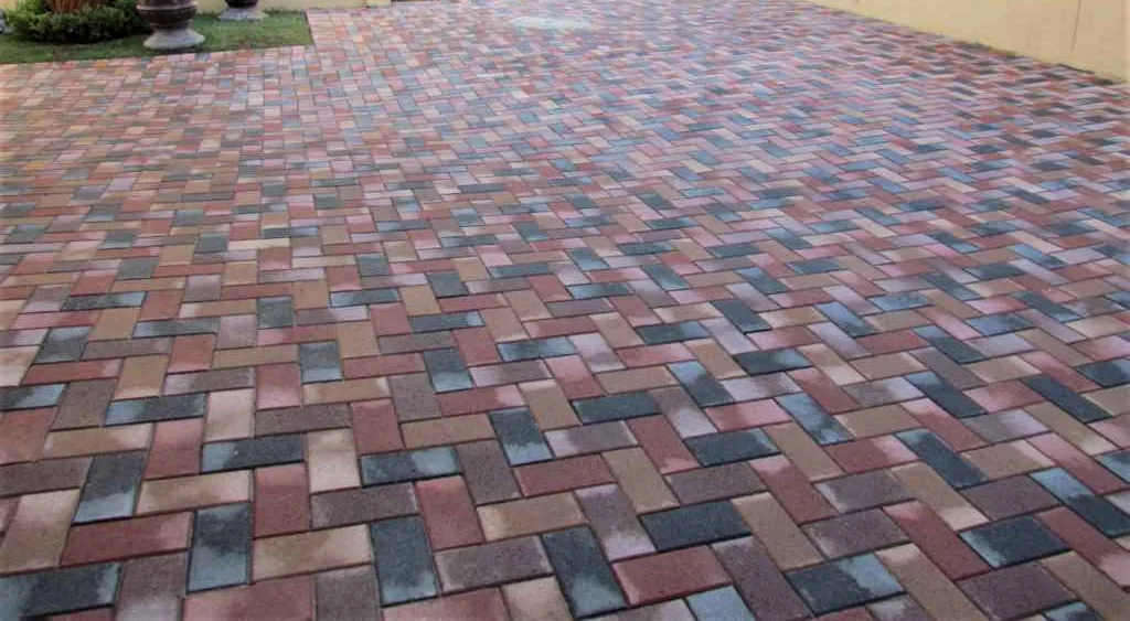 Driveway Paving: Materials, Costs and What to Expect 3 Multi-tone red, tan and slate-grey concrete pavers laid in a herringbone weave across a residential driveway, joints filled and the surface swept