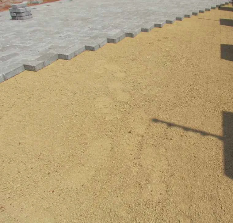 Driveway Paving: Materials, Costs and What to Expect 2 Grey concrete pavers laid up to a stepped leading edge, standing against an open bed of screeded sand that has not yet been built on