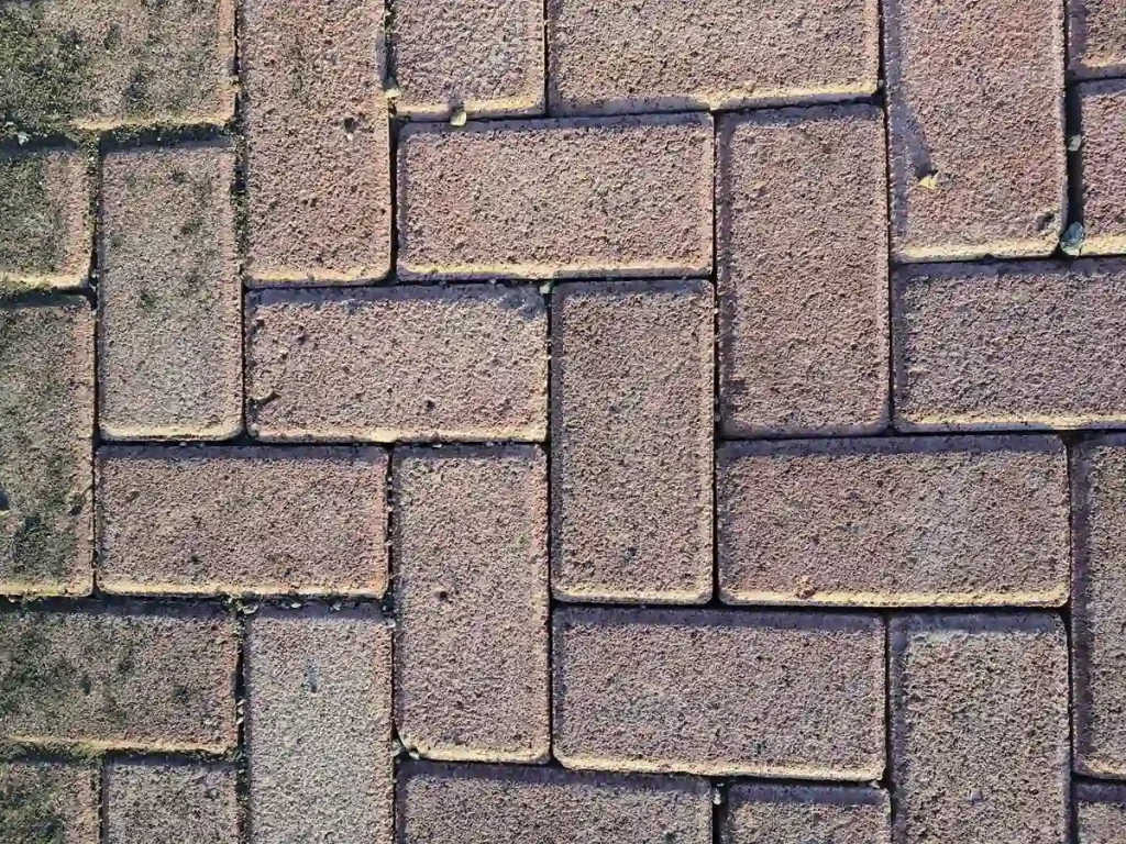 paint-post-faded-paving-worn-colour Close-up of brick-format paving with the colour worn chalky and patchy, and pale sand packed into every joint