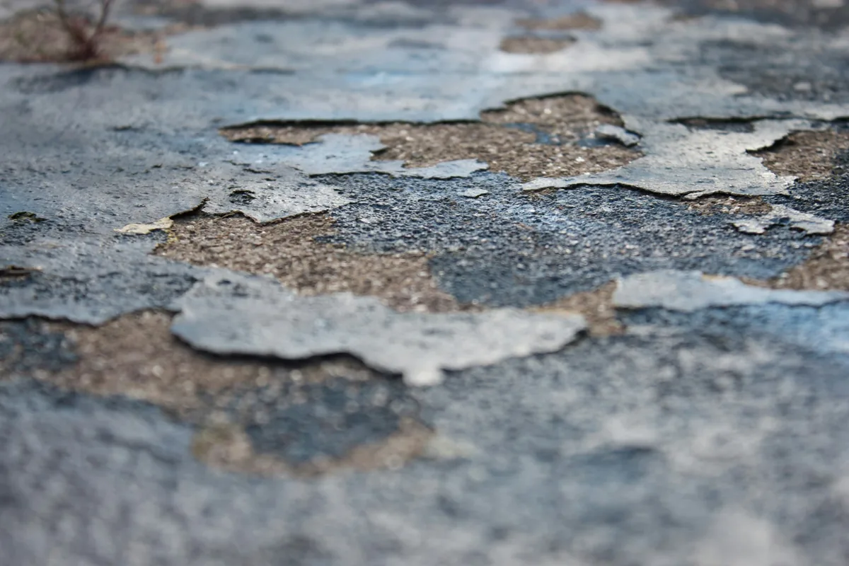Can You Paint Paving Bricks? What Works and What Peels 2 Grey paint lifting away from an outdoor ground surface in thin curling flakes, exposing the coarse substrate underneath