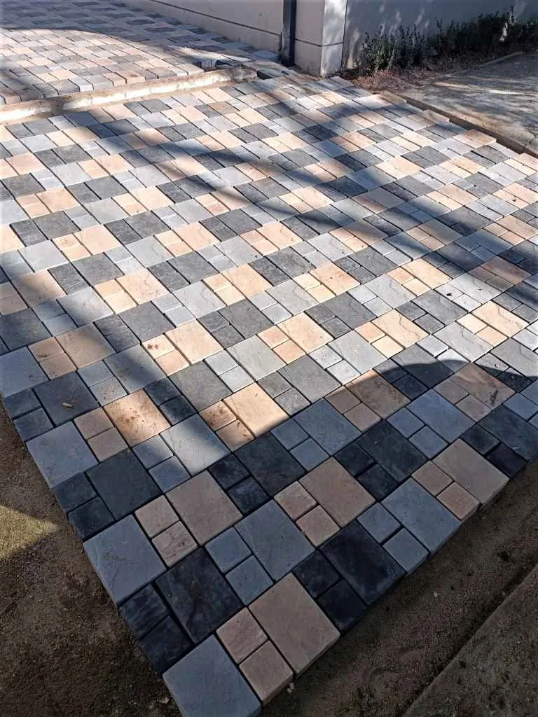 Types of Paving Bricks in South Africa 1 Paving laid in a mix of square and rectangular units in charcoal, pale grey and sand tones, with a border band combining three different unit sizes along the edge of the field